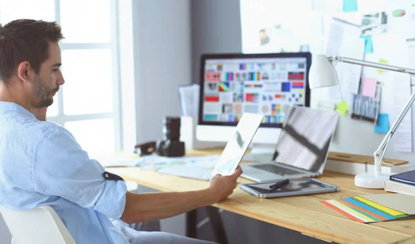 Retrato del joven diseñador sentado en el estudio gráfico frente a la computadora portátil y el ordenador mientras trabaja en línea. — Foto de Stock