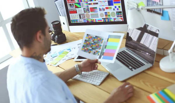 Retrato del joven diseñador sentado en el estudio gráfico frente a la computadora portátil y el ordenador mientras trabaja en línea. — Foto de Stock