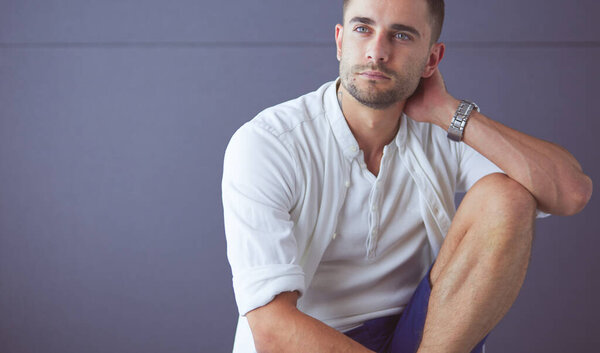 Young businessman sitting isolated on grey background.