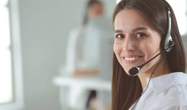 Mujer de negocios sonriente u operador de línea de ayuda con auriculares y computadora en la oficina — Foto de Stock