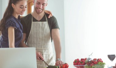 Sebze doğrayan genç bir adam ve mutfakta dizüstü bilgisayarı olan bir kadın.