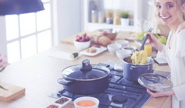 Evdeki mutfakta yemek pişiren güzel genç bir kadın.