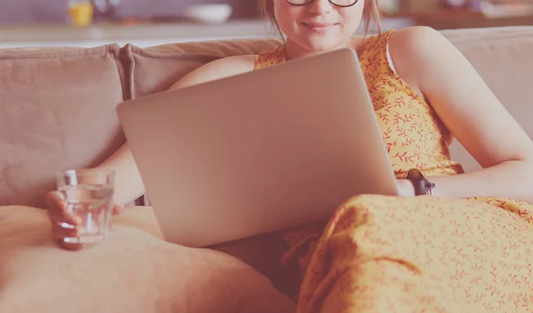 아름다운 젊은 여성이 소파에 앉아서 노트북을 만들고 있습니다. — 스톡 사진