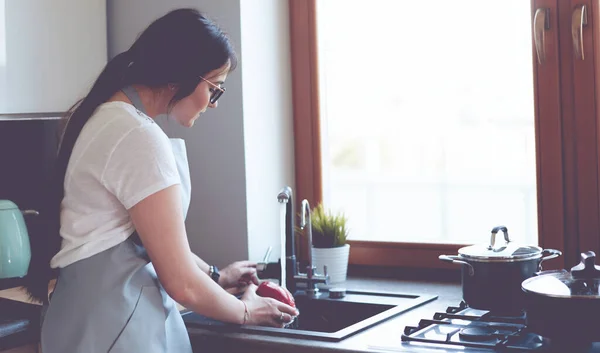 Een vrouw die groenten wast. mooie jonge vrouw wassen groenten voor salade en glimlachen terwijl staan in de keuken — Stockfoto