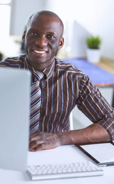 Knappe Afro-Amerikaans zakenman in klassieke pak is met behulp van een laptop en glimlachen terwijl u werkt in office — Stockfoto