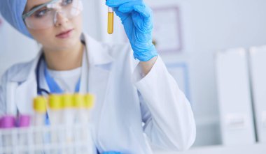 Bir kadın tıbbi veya bilimsel araştırmacı ya da kadın doktor laboratuarda bir test tüpü dolusu temiz çözeltiye bakıyor. .