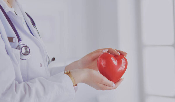 Женщина-врач со стетоскопом, держащая сердце на светлом фоне.