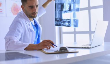 Yakışıklı doktor genç bayan hastasıyla konuşuyor ve ofisinde otururken notlar alıyor.