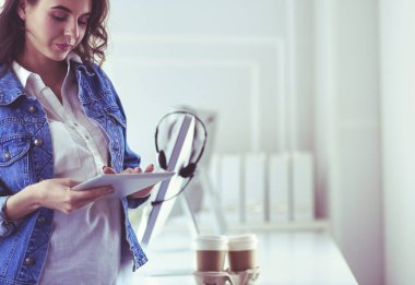 Gülümseyen kadın kahve içiyor ve kafede tablet kullanıyor.