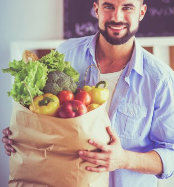 Mutfak arka planında poşet dolusu erzak tutan adam. Alışveriş ve sağlıklı gıda konsepti.