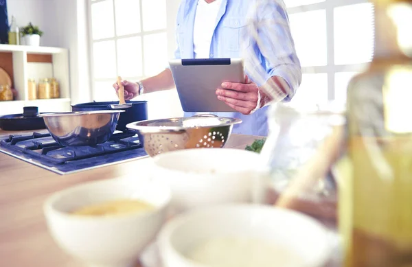 Man following recipe on digital tablet and cooking tasty and healthy food in kitchen at home.