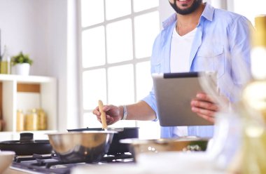 Dijital tablet ve yemek pişirme tarifine uyan bir adam evdeki mutfakta lezzetli ve sağlıklı yemekler pişiriyor..