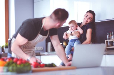 Masadaki dizüstü bilgisayara bakarken mutfakta sebze pişiren adamın portresi..
