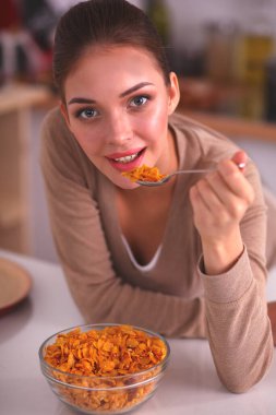 Gülümseyen kadın mutfağın içinde kahvaltı yapıyor.