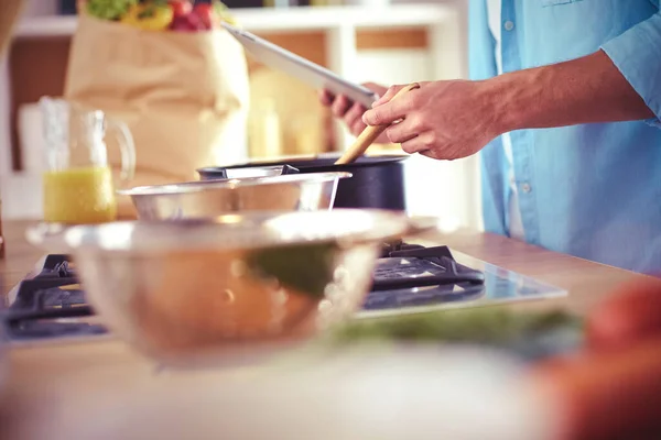 Man following recipe on digital tablet and cooking tasty and healthy food in kitchen at home.