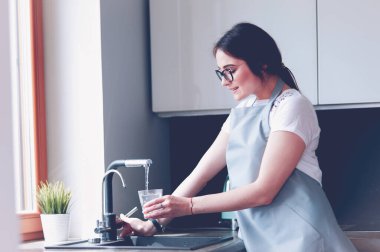 İnsan eli bardağı tutuyor. Mutfak musluğunda taze su dökülüyor..