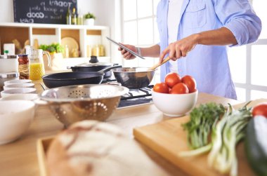 Dijital tablet ve yemek pişirme tarifine uyan bir adam evdeki mutfakta lezzetli ve sağlıklı yemekler pişiriyor..