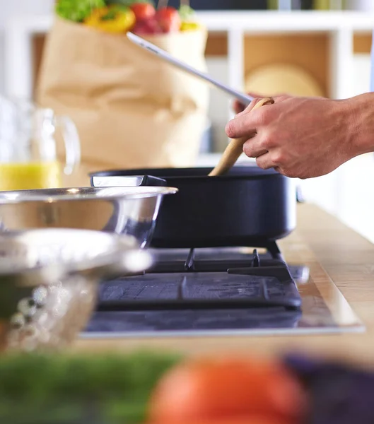 Man following recipe on digital tablet and cooking tasty and healthy food in kitchen at home.