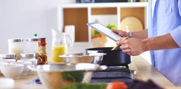 Man following recipe on digital tablet and cooking tasty and healthy food in kitchen at home.