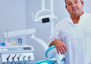 Diş kliniğinde duran gülümseyen bir dişçinin portresi..