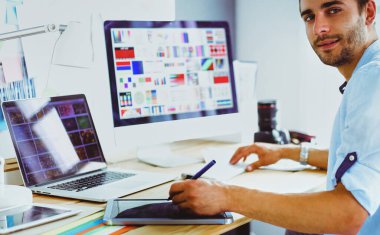 İnternette çalışırken bilgisayarın ve dizüstü bilgisayarın önünde grafik stüdyosunda oturan genç tasarımcının portresi