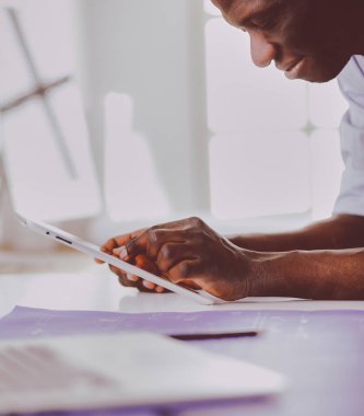 Ofiste bilgisayar ve planlarla çalışan Afrikalı Amerikalı bir mimar..