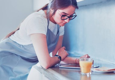 Mutfaktaki genç, beyaz tenli esmer ev kadınının portresi. Sabah bir fincan kahve ve tabletle.