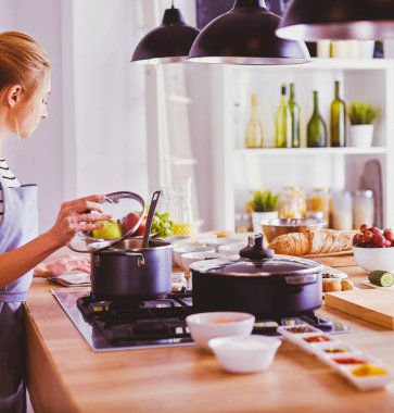 Evdeki mutfakta yemek pişiren güzel genç bir kadın..