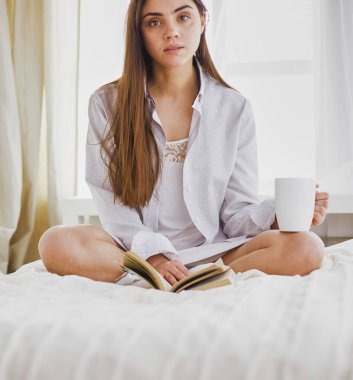 Yatakta oturup kitap okuyan ve kahvaltı yapan bir kadın..