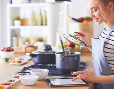 Mutfakta yemek yapmak için tablet bilgisayar kullanan genç bir kadın..