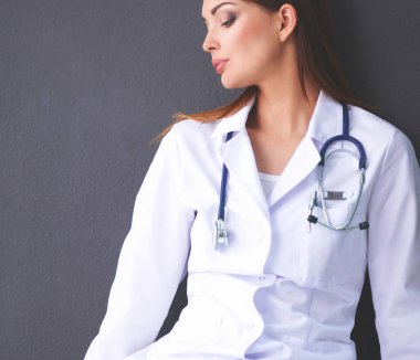 Gri arka planda oturan bir kadın doktor.