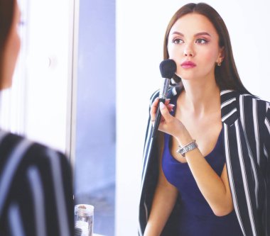 Güzellik kadını makyaj uygulamak. Aynaya bakıyorum ve büyük bir fırça ile kozmetik uygulama güzel kız.