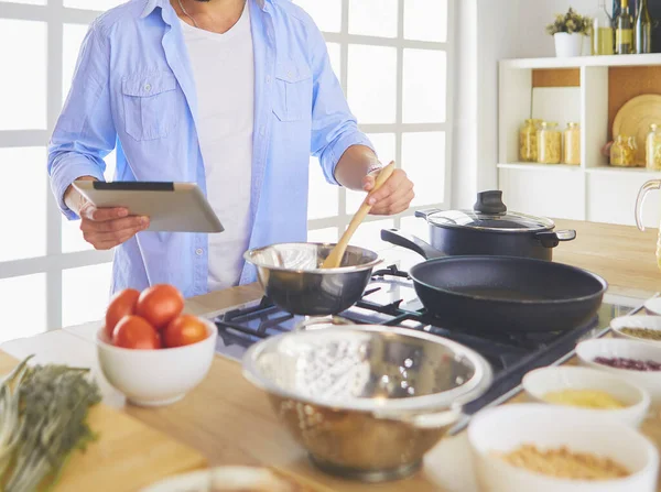 Man following recipe on digital tablet and cooking tasty and healthy food in kitchen at home.