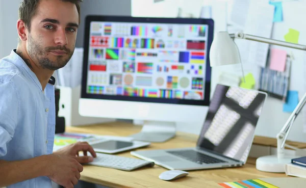 Portrait of young designer sitting at graphic studio in front of laptop and computer while working online