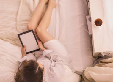 Sabahları yatakta otururken tablet kullanan ve kahve içen kadın portresi.