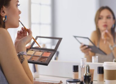 Esmer bir kadın aynanın önünde akşam randevusunu telafi etmek için başvuruyor..