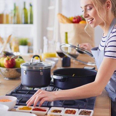 Evdeki mutfakta yemek pişiren güzel genç bir kadın..