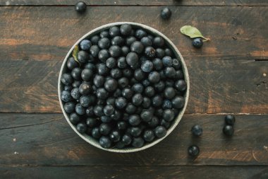 Koyu kırsal ahşap masa zemininde siyah mavimsi meyveli bir kase. 