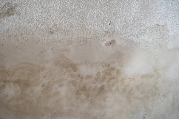 Cement render plaster coating with damp stain on old popcorn ceiling wall with bumpy texture