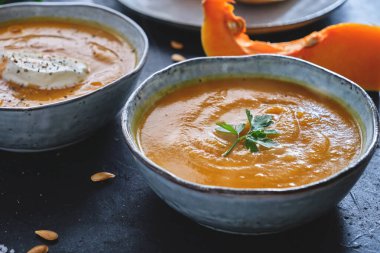 Ev yapımı kavrulmuş kabak kremalı çorba. Üstünde maydanoz yaprağı ve kabak parçaları ve siyah mutfak masasının üzerinde tohumlar var. 