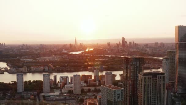 Vista panorâmica aérea da cidade contra o pôr-do-sol, arranha-céus do centro da cidade à distância. Filmagem decrescente revela o topo do prédio cilíndrico de apartamentos da Arena Tower. Londres, Reino Unido — Vídeo de Stock