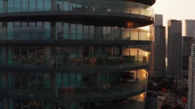 Camdan duvarları olan uzun, modern bir bina. İş merkezindeki gökdelenleri gün batımına karşı gözler önüne sermek. Londra, İngiltere