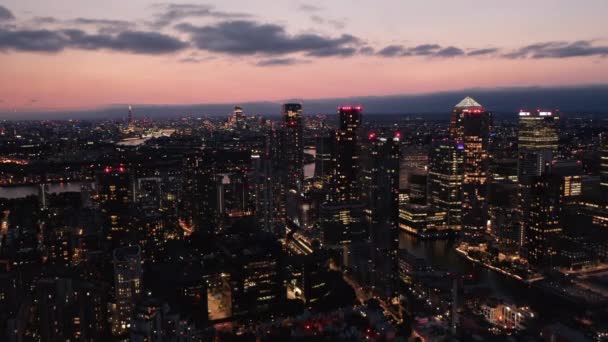 Піднятий погляд на сучасні високі будівлі в фінансовому центрі Canary Wharf в сутінках. Освітлене нічне місто з висоти. Лондон, Велика Британія — стокове відео
