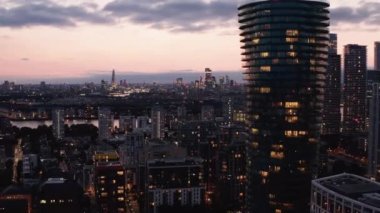 Forvetler Arena Kulesi 'nin etrafında uçuyor. Uzun, modern silindirik apartman dairesi. Şehir alacakaranlık gökyüzüne karşı. Londra, İngiltere