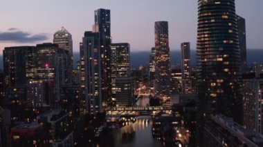 Canary Wharf iş merkezindeki su yüzeyine iniş görüntüleri. Gün batımından sonra gökdelenlerin ışıklı pencereleri. Londra, İngiltere