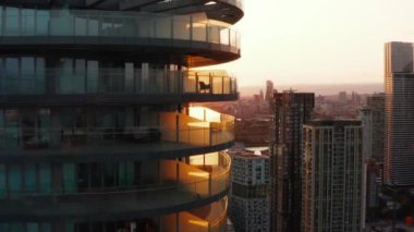 Etrafı teraslarla çevrili, yüksek, yuvarlak apartman dairesinin yükselen görüntüsü. Batan güneşe karşı şehir manzarası ortaya çıkıyor. Londra, İngiltere