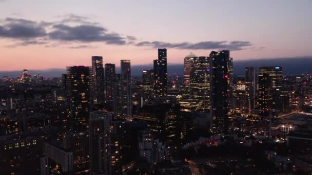 Ascending footage of skyscrapers in Canary Wharf business centre at dusk. Tall illuminated buildings against pink twilight sky. London, UK — Stock Video