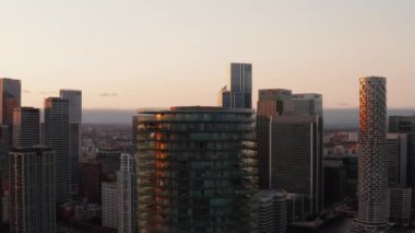 Baltimore Kulesi 'nin kaydırak ve pan görüntüleri. Halkalarında teraslar olan silindirik bir apartman dairesi. Canary Wharf ilçesindeki gökdelenler ve gün batımında şehir manzarası. Londra, İngiltere
