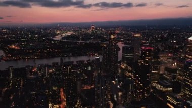 İleri, gece kasabasının üzerinde uçar. Aydınlatılmış sokaklar ve binalar. Gün batımından sonra renkli gökyüzüne karşı şehir manzarası. Londra, İngiltere