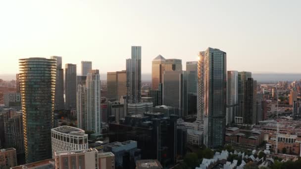 Stigande skott av höga kontorsbyggnader i affärscentrum Canary Wharf. Lit från sidan genom att gå ner i solen. Skyskrapor i gyllene timmen. London, Förenade kungariket — Stockvideo